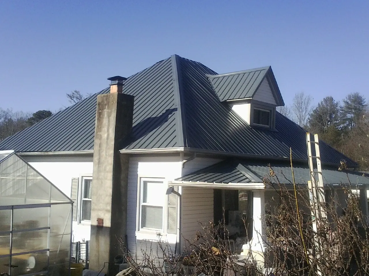 Dark blue standing seam metal roof on a white farmhouse with dormer — Slate & Tile Roof Repair by Roofing Brothers in Morrilton