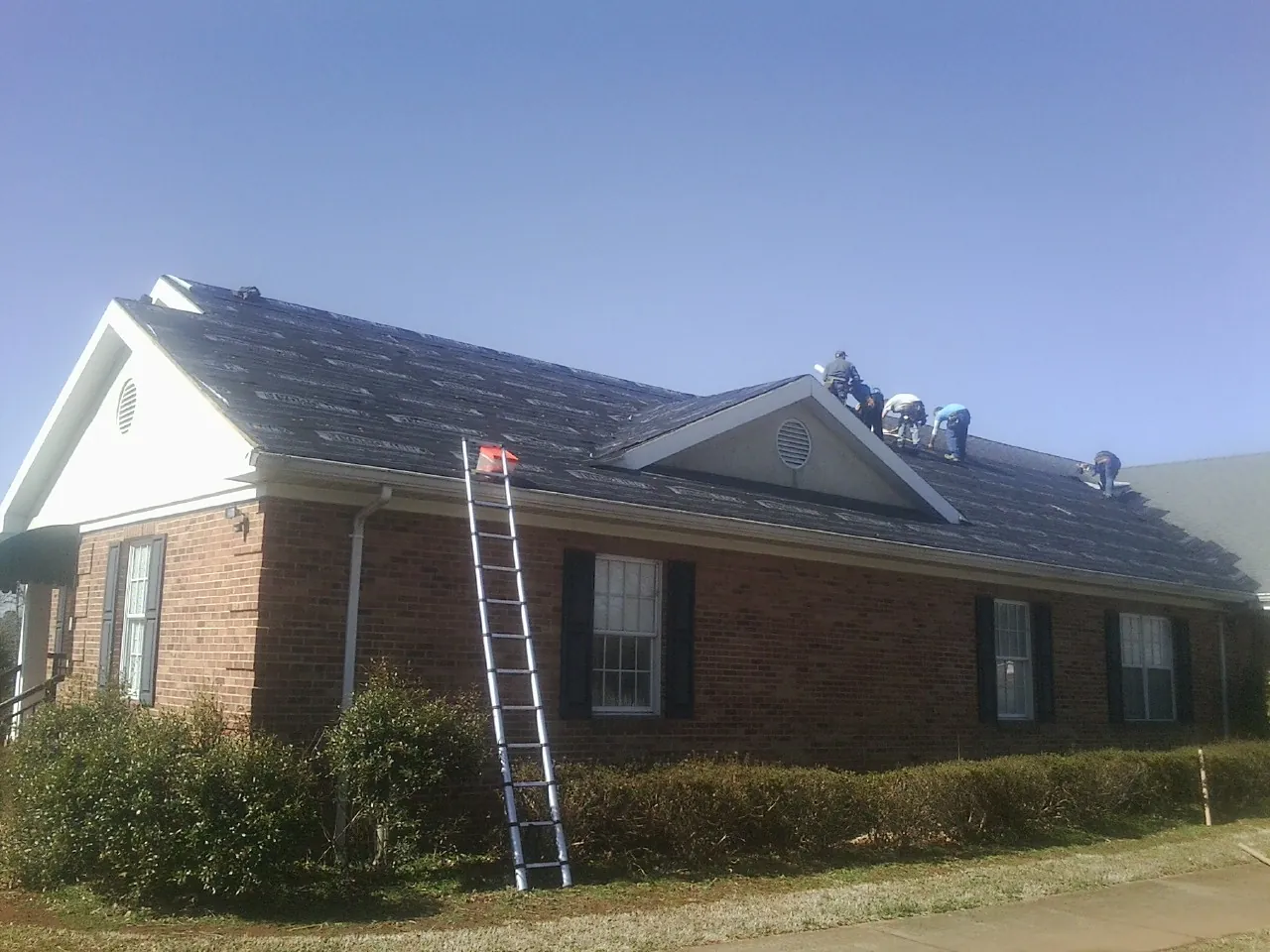 Crew tearing shingles off a brick ranch roof with a ladder set — Emergency Roof Repair work by our crew in Morrilton