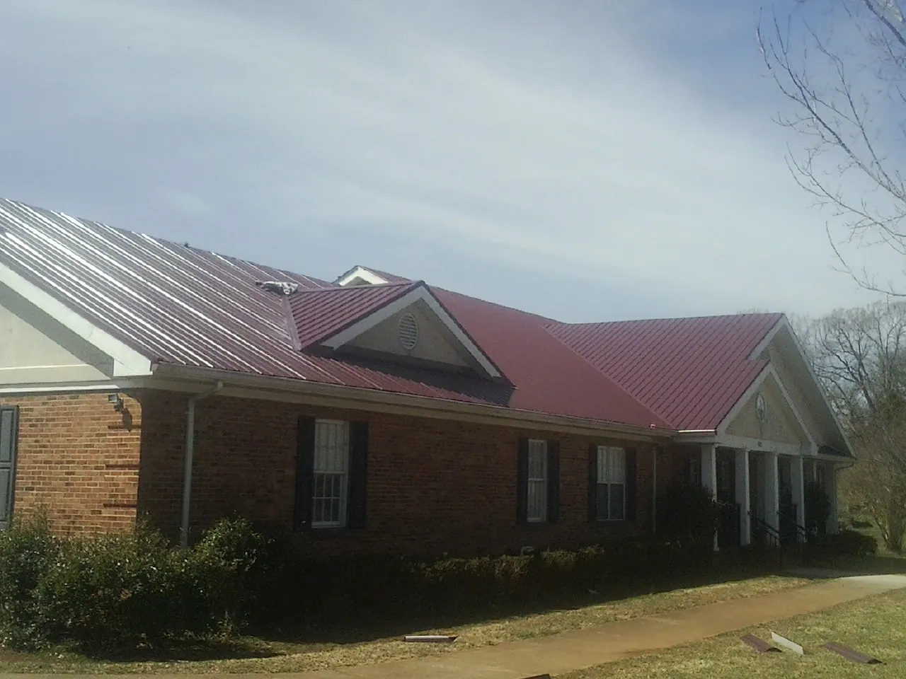 Red metal roof with gabled entries on a long brick building, from a Hail Damage Roof Repair job in Morrilton