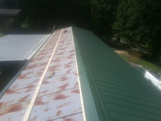 Old rusted panels beside newly installed green metal roofing — Wind Damage Roof Repair by Roofing Brothers in Morrilton
