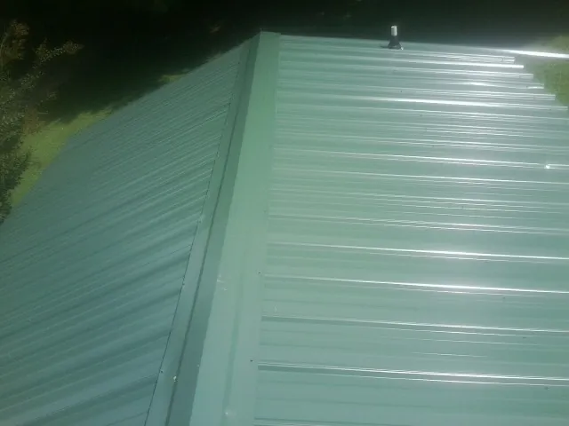 New green metal panels meeting at the ridge of a roof — Flat Roof Repair work by our crew in Morrilton