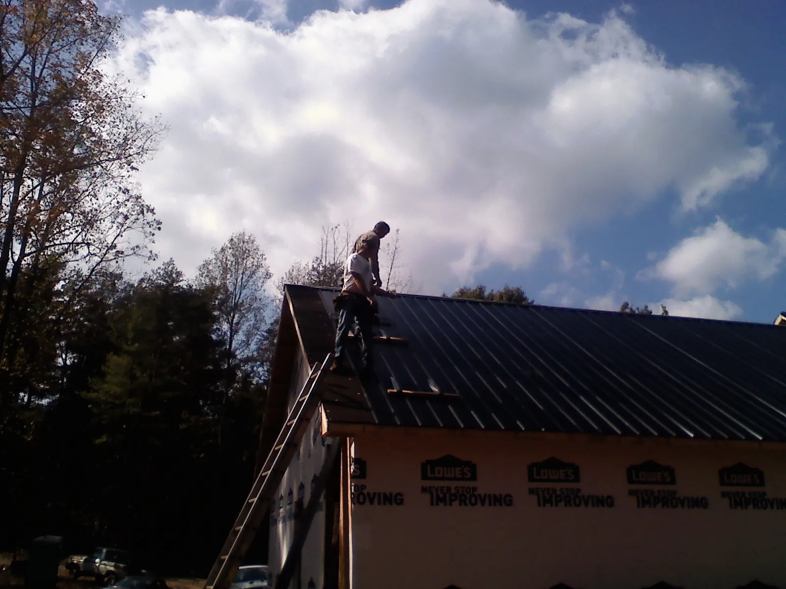 Roofer fastening dark metal panels high against a cloudy sky, from a Roof Inspection job in Morrilton