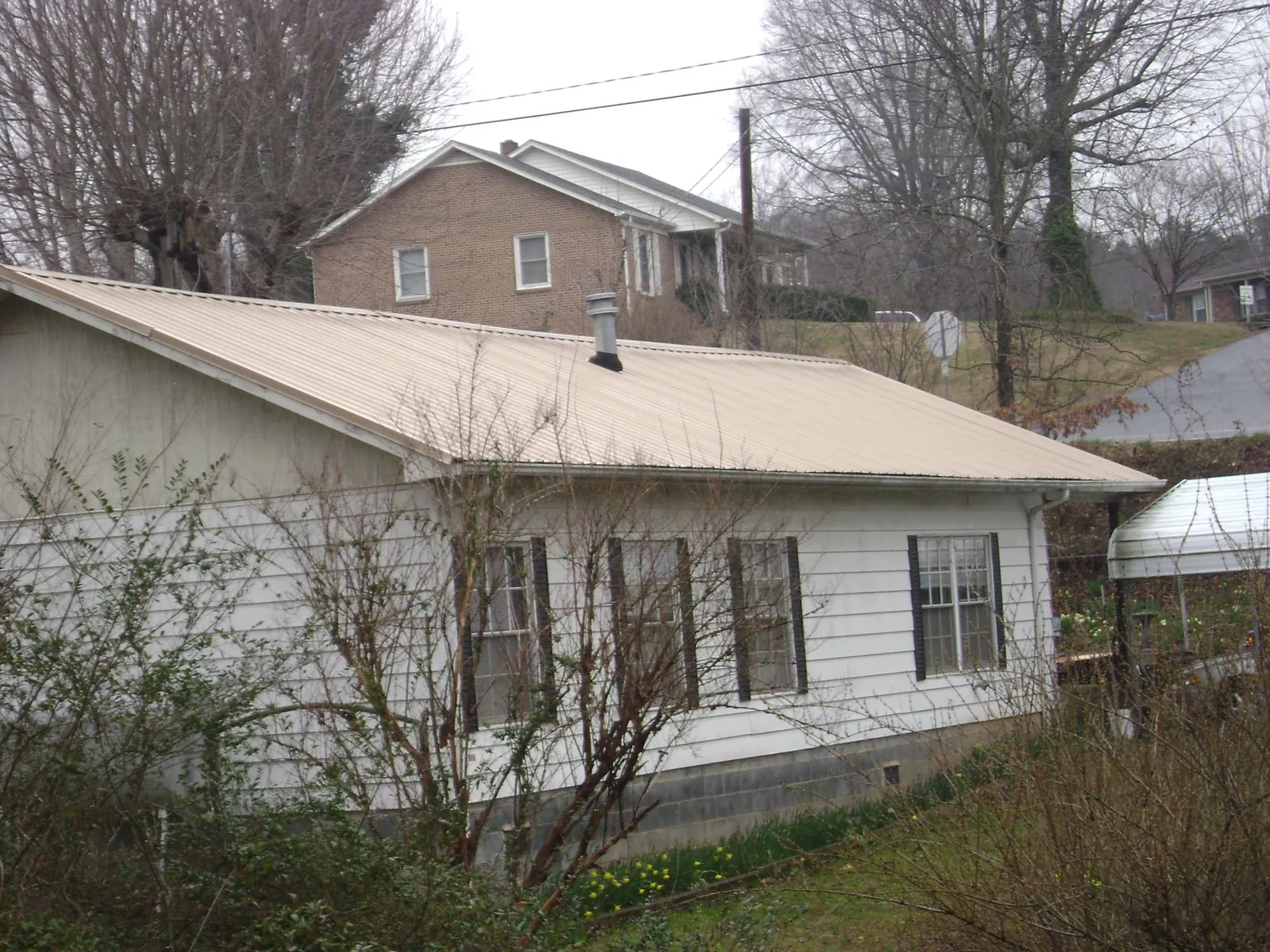 Tan metal roof on a white sided house set into a hillside — Commercial Roofing by Roofing Brothers in Morrilton