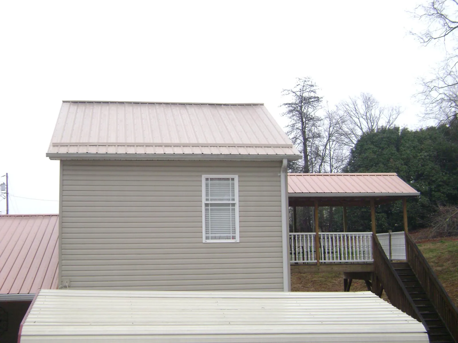 Tan metal roofs on a two story addition and attached porch, from a Roof Replacement job in Morrilton